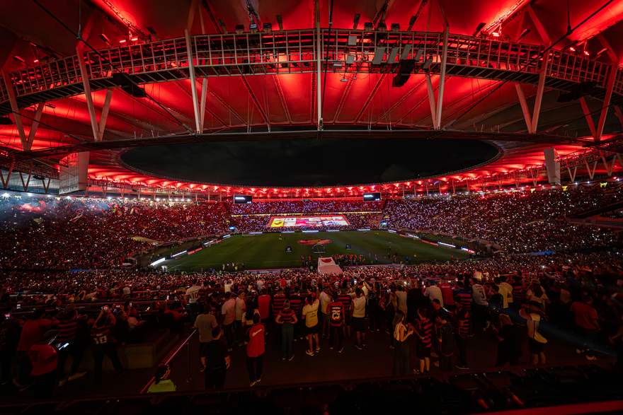 Mosaico de criações da torcida projetado no bandeirão sob o teto vermelho do Maracanã